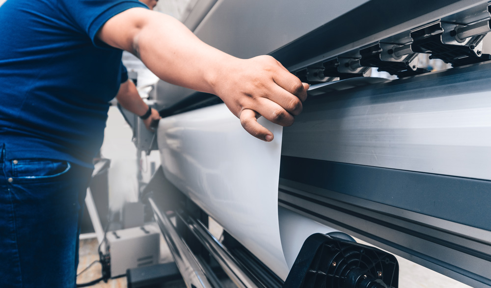 man-holding-printable-material-on-alarge-format-printing-plotter